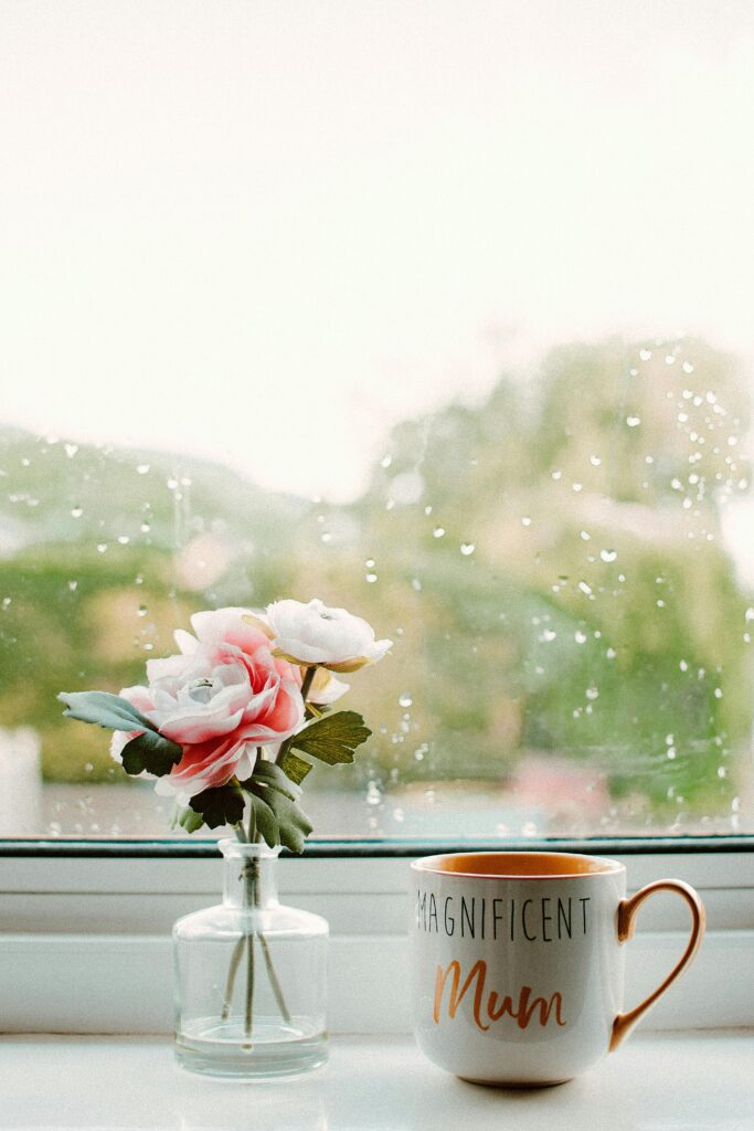 A relaxing scene with a 'magnificent mum' mug and flowers by a rainy window.